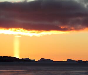 A “solar pillar” phenomenon where there appears to be a thick beam of light between the sun at sunset and the clouds above it. Rather like a chimney coming up from the sun.