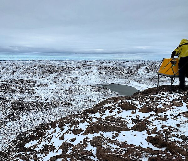 A man overlooks a snow-covered valley from a rocky outcrop